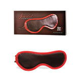 Displayed against a white background, the Adam & Eve Scarlet Couture Blindfold is black with red trim, made from vegan leather, featuring an adjustable strap. The box reads Scarlet Couture Bondage and Adam & Eve Blindfold with a heart logo. Ideal for enhancing bondage play.