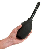 A hand holds the Adam & Eve Ez Anal Douche, a black bulb-shaped device with a tube-like nozzle. The ribbed design provides grip, and its long, narrow nozzle allows precision similar to an antibacterial cleaner, ideal for delicate equipment. The background is plain white.