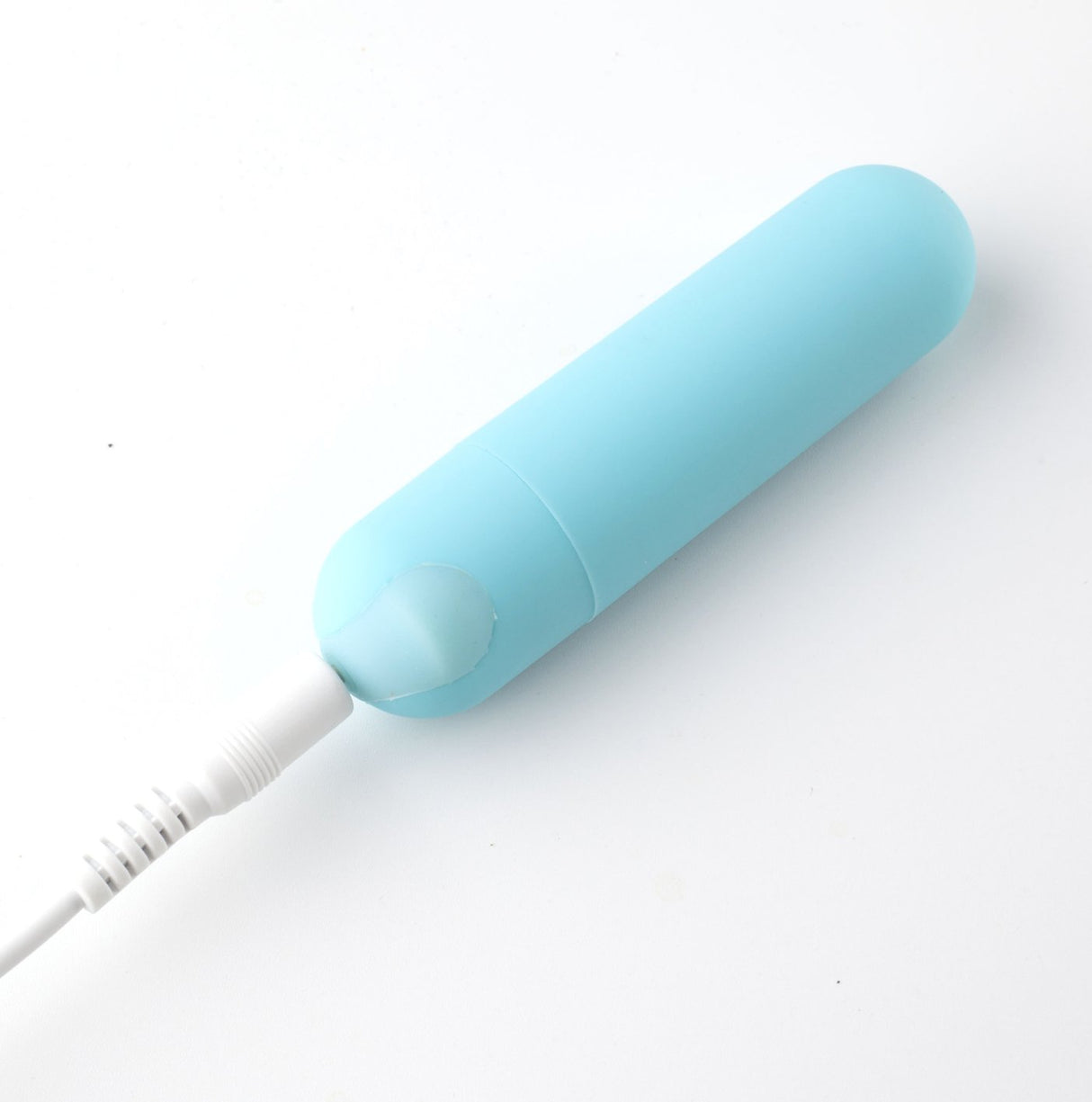 The Maia Jessi, a teal blue 7.6 cm USB rechargeable bullet vibrator, features a smooth silicone finish and a slightly tapered design at the connection point. It includes a white cord plugged into its rounded end and is set against a plain white background.