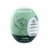 The Satisfyer Masturbator Egg - Riffle, designed as a travel-friendly white stroker sleeve, comes in green-and-black packaging featuring a relaxed face drawing and a circular cutout revealing the cyber-skin texture. Branding details are printed in white at the top and bottom.