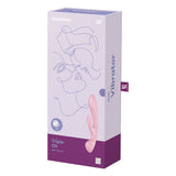 The image showcases the box of the Satisfyer Triple Oh - Pink USB Rechargeable Rabbit Vibrator, featuring abstract face line art and branding. The purple and white packaging prominently displays its name, highlighting a light pink, curvy vibe made from body-safe silicone.