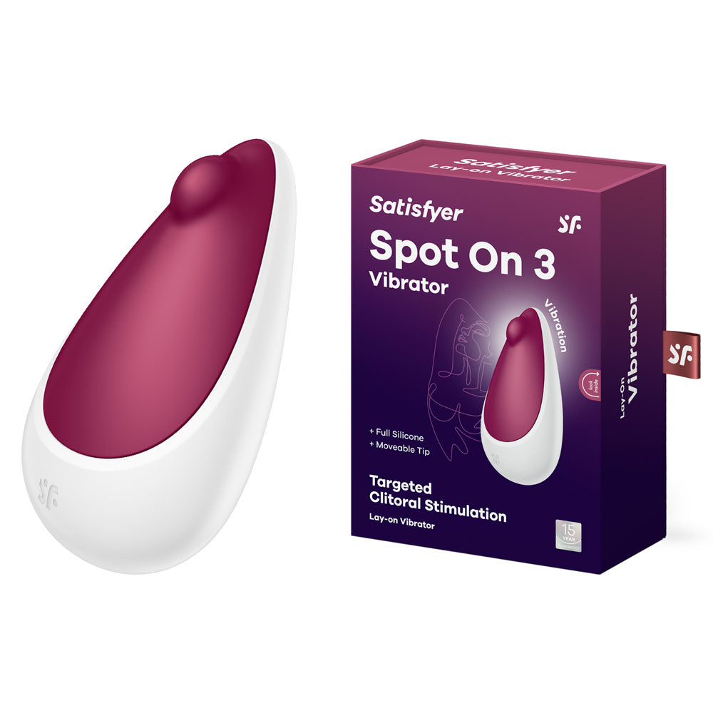 The packaging of the Satisfyer Spot On 3 - Berry USB Rechargeable Stimulator highlights its smooth, ergonomic design. The burgundy silicone vibrator with a white base is portrayed in a dark purple box that emphasizes its features, including targeted clitoral stimulation and waterproof, rechargeable capabilities.