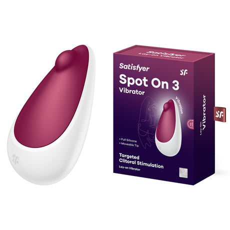 The packaging of the Satisfyer Spot On 3 - Berry USB Rechargeable Stimulator highlights its smooth, ergonomic design. The burgundy silicone vibrator with a white base is portrayed in a dark purple box that emphasizes its features, including targeted clitoral stimulation and waterproof, rechargeable capabilities.