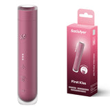 The Satisfyer First Kiss - Pink USB Rechargeable Air Pulse Stimulator, a compact cylindrical device with silicone coating and button icons, features three light indicators. The packaging emphasizes its travel size, USB-C rechargeability, and adjustable pressure wave Air Pulse Vibrator technology.