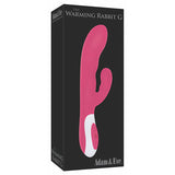 The box for Adam & Eve The Warming Rabbit G - Pink 21.6 cm shows a pink dual-stimulation massager with a G-Spot tip and warming vibrator, resting on a white base with buttons against a black background. The brand name is in white text.