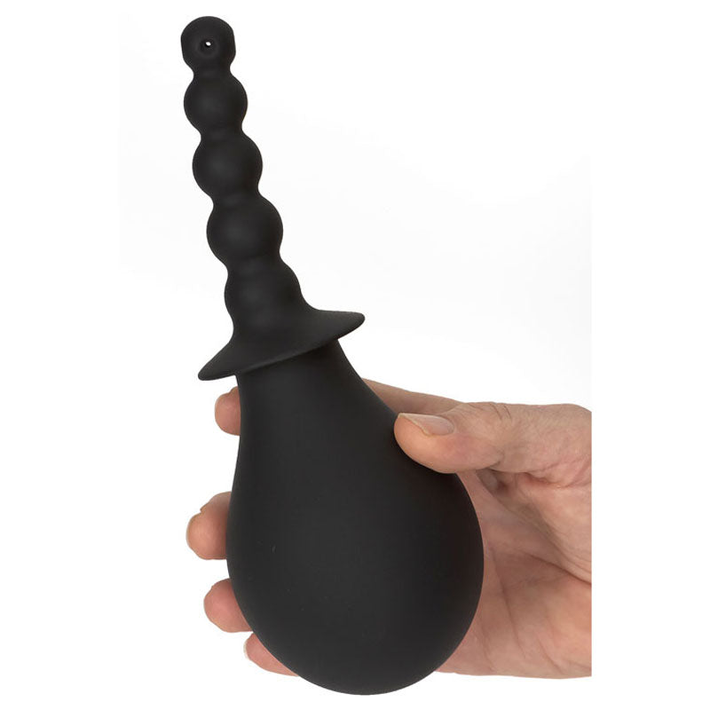 A hand holds the Adam & Eve Smooth & Easy Silicone Douche - Black Douche, featuring a black rubber bulb and a textured silicone tip with spherical protrusions for anal douching. Its pear-shaped design ensures easy cleaning, set against a plain white background.