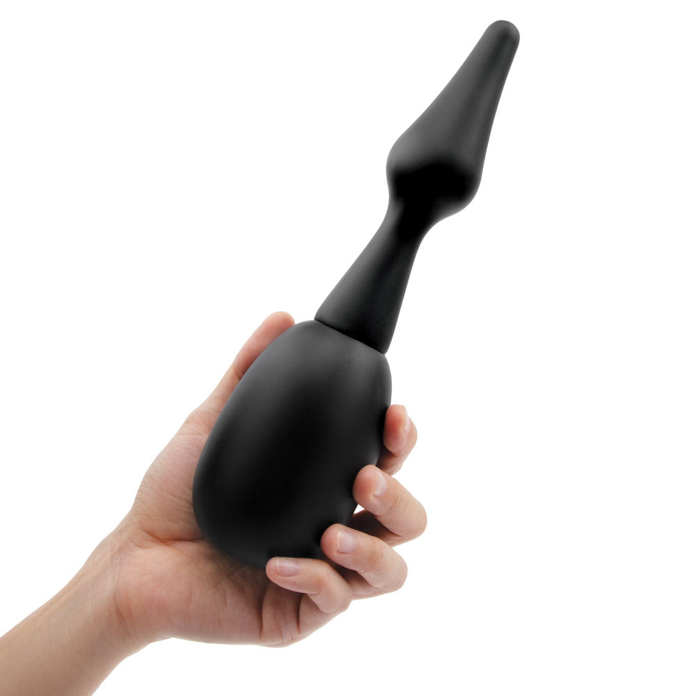 A hand displays the AquaClean Silicone 1-Way Valve Douche Set with a sleek black design, hypoallergenic materials, and a long tapered nozzle. The smooth matte finish allows easy handling against a white backdrop. It includes a butt plug nozzle and comes with a free travel douche.