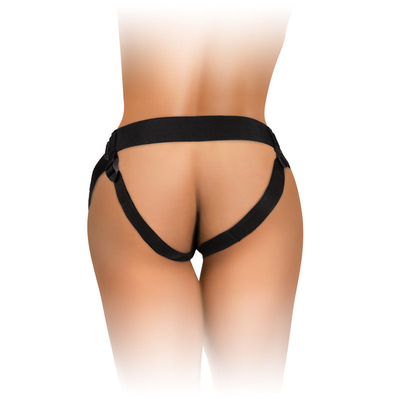 A person wears the King Cock Elite Comfy Body Dock Strap-On Harness in black, featuring adjustable straps around the waist and thighs. Its minimal design highlights the back and legs with a softly blurred background focusing on the lower body.