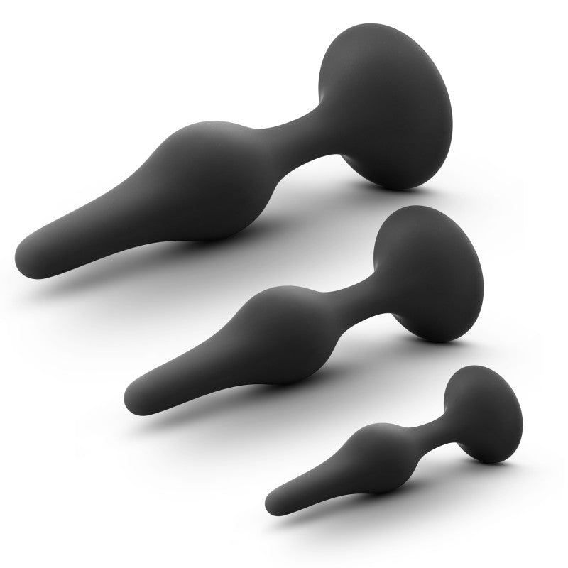 The Anal Adventures Platinum Silicone Beginner Plug Kit includes three black butt plugs, displayed diagonally on a white backdrop. Each plug features StayPut™ technology, a tapered shape, and a wide base for safe anal exploration from the largest to smallest sizes.