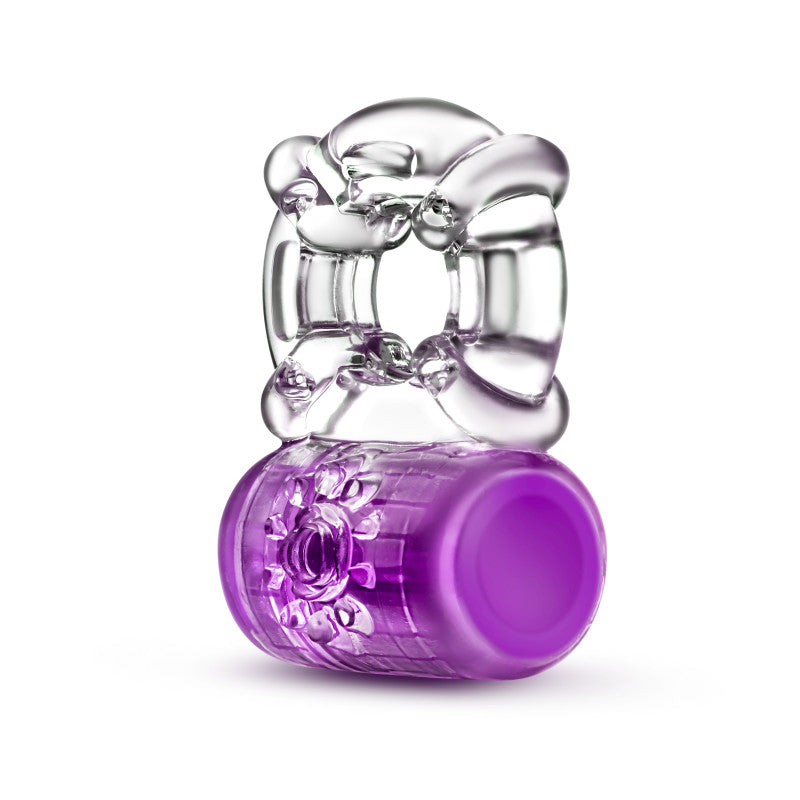 The Play With Me Pleaser Rechargeable C-Ring features a clear, textured ring on a purple floral-patterned cylindrical base. USB rechargeable, it combines geometric and decorative elements with powerful vibrations for an artistic and functional experience reminiscent of vibrating C-rings.