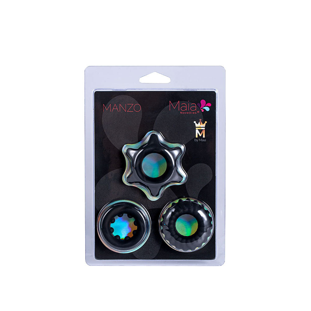 The Maia MANZO set includes three metallic, rainbow-centered silicone cock rings on a black backing, featuring Manzo and Maia branding with a stylized logo and floral designs. Each ring boasts a unique design and texture.