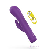 The Bwild Bunny Infinite Deluxe, a purple 19.3 cm USB rechargeable rabbit vibrator, features a dual-motor design with a curved form and protruding clitoral stimulator. It includes three control buttons and comes with a yellow USB charging cable, showcasing the bswish brand on a white background.