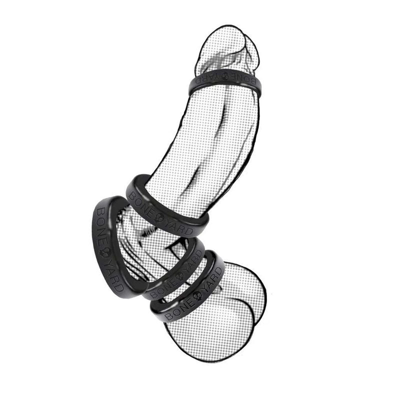 A Boneyard Silicone Ring 30mm in black, inscribed with BONE YARD, adorns a phallus-shaped fishnet-like mesh sculpture. Rings placed at the base and midway create contrasting textures and patterns, typical of artistic man toys.