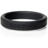 The Boneyard Silicone Ring 50mm - Black Cock Ring is a matte black silicone accessory embossed with BONE YARD and a skull icon. It features 3x-stretch flexibility for comfort, making it an ideal addition to the man toys collection, elegantly displayed against a white backdrop.