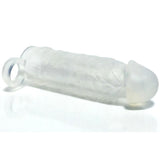 The Boneyard Meaty Cock Extender - Clear is a translucent silicone sleeve with a phallic shape that serves as a penis extender. It features textured ribbing along the shaft for enhanced sensation, has a rounded tip, and includes a loop at the end, lying on a plain white surface.