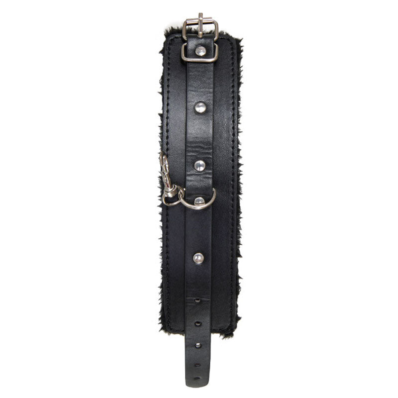 The Adam & Eve Hog Tie is a sleek black cuff made of vegan leather, adorned with metal studs and a buckle. Featuring soft, fur-like lining for comfort, it has a sturdy D-ring with an attached clip and adjustable strap holes for secure wrist or ankle restraint.