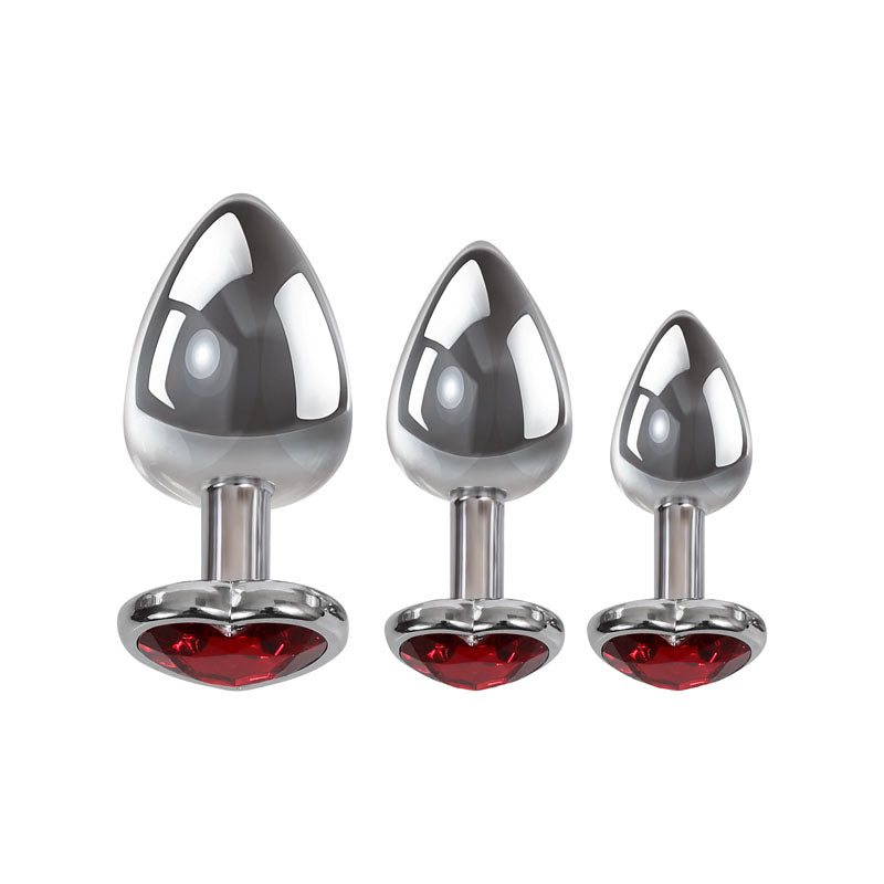 The Adam & Eve Three Hearts Gem Anal Plug Set features three metallic, conical anal plugs in varying sizes. Each plug has a reflective silver finish and is adorned with vibrant red, heart-shaped jeweled bases for an elegant addition to any collection.