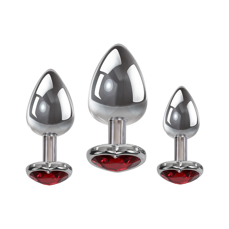 The Adam & Eve Three Hearts Gem Anal Plug Set includes three metallic butt plugs, each with a reflective silver finish and jeweled red heart base. Displayed symmetrically from smallest to largest against a white background, they are visually striking and functional for anal pleasure.