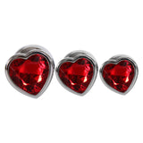 The Adam & Eve Three Hearts Gem Anal Plug Set features three silver heart-shaped metal plugs with vibrant red gemstone centers, arranged side by side in varying sizes from large to small; perfect for anal training enthusiasts with their polished edges and sparkling facets.