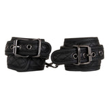 The Adam & Eve Fetish Dreams Beginner Bondage Set features black quilted vegan leather handcuffs with metal buckles, rivet detailing, and adjustable straps linked by a short metal chain with a clip, offering a sleek and sturdy look for erotic restraint play.