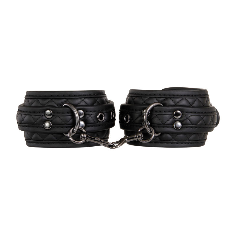 The Adam & Eve Fetish Dreams Beginner Bondage Set includes two black vegan leather wrist cuffs with quilted stitching and metallic studs, linked by a short chain with metal clasps. This sturdy and stylish set is ideal for exploring erotic restraint play.