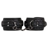 The Adam & Eve Fetish Dreams Advanced Bondage Set is a sleek and modern vegan leather set featuring black quilted adjustable cuffs linked by a central chain, with diagonal stitching, metal eyelets, and shiny accents enhancing its textured design.