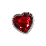 The Adam & Eve Red Heart Gem Anal Plug features a red heart-shaped faceted gemstone set in a shiny silver frame, creating bright highlights and deep shadows. Its polished contrast adds allure against the plain white background.