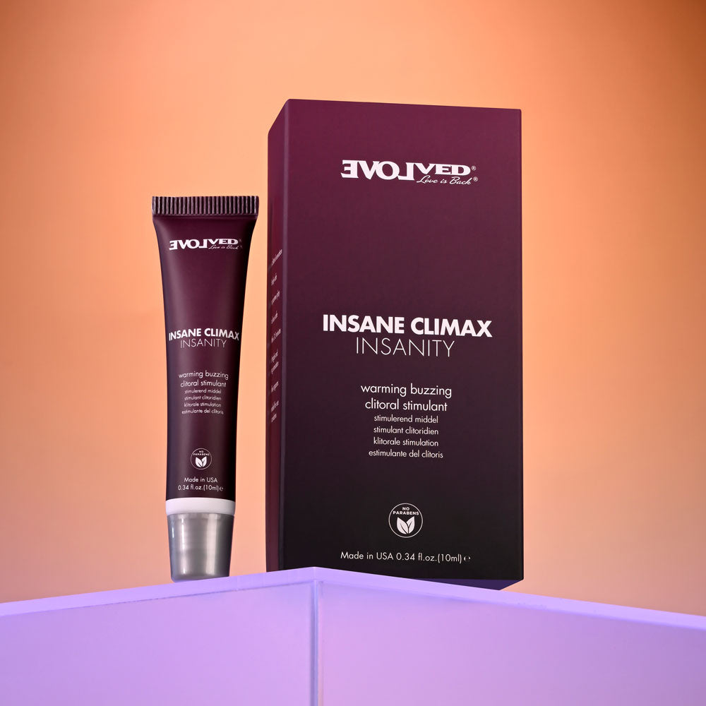 A small, sleek tube of Evolved INSANE CLIMAX - INSANITY Warming Buzzing Clitoral Stimulation Gel, 10 ml, sits beside its matching box on a glowing lavender surface. The modern packaging promises a warming, tingling sensation for clitoral stimulation.