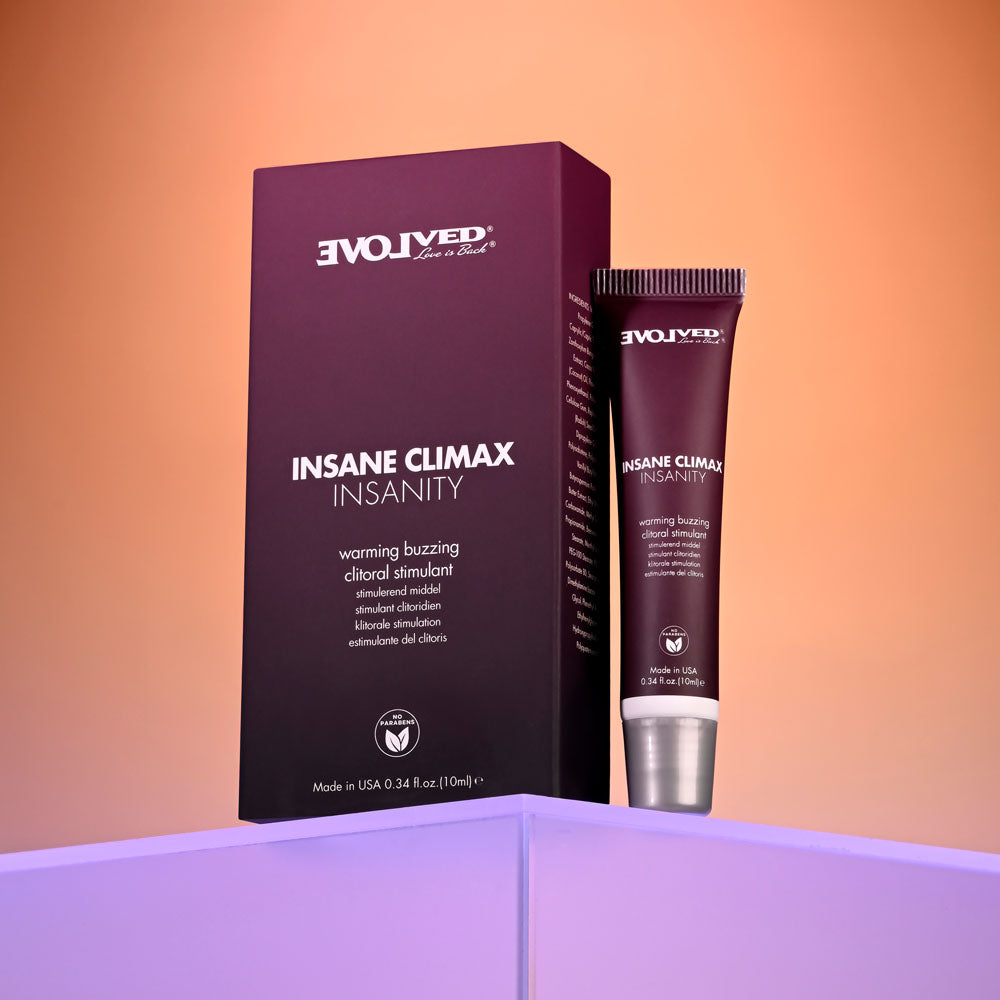 A tube of Evolved INSANE CLIMAX - INSANITY clitoral stimulant with warming and buzzing effects stands beside its box on a reflective pink-purple surface, showcasing dark purple packaging with white text against an orange gradient background.