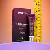 A small tube labeled Evolved INSANE CLIMAX - INSANITY stands before its maroon box, promising warming and buzzing sensations. A yellow tape is partially unfurled beside them against a purple-to-orange backdrop on a purple platform, introducing itself as a clitoral stimulant gel.