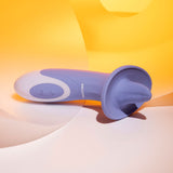 The Evolved LIX & KISSES, a purple 18.7 cm USB rechargeable flicking tongue stimulator with ergonomic design and multiple vibrating speeds, stands out against soft curved light orange and white surfaces. Subtle shadows and reflections enhance its modern, sleek aesthetic.