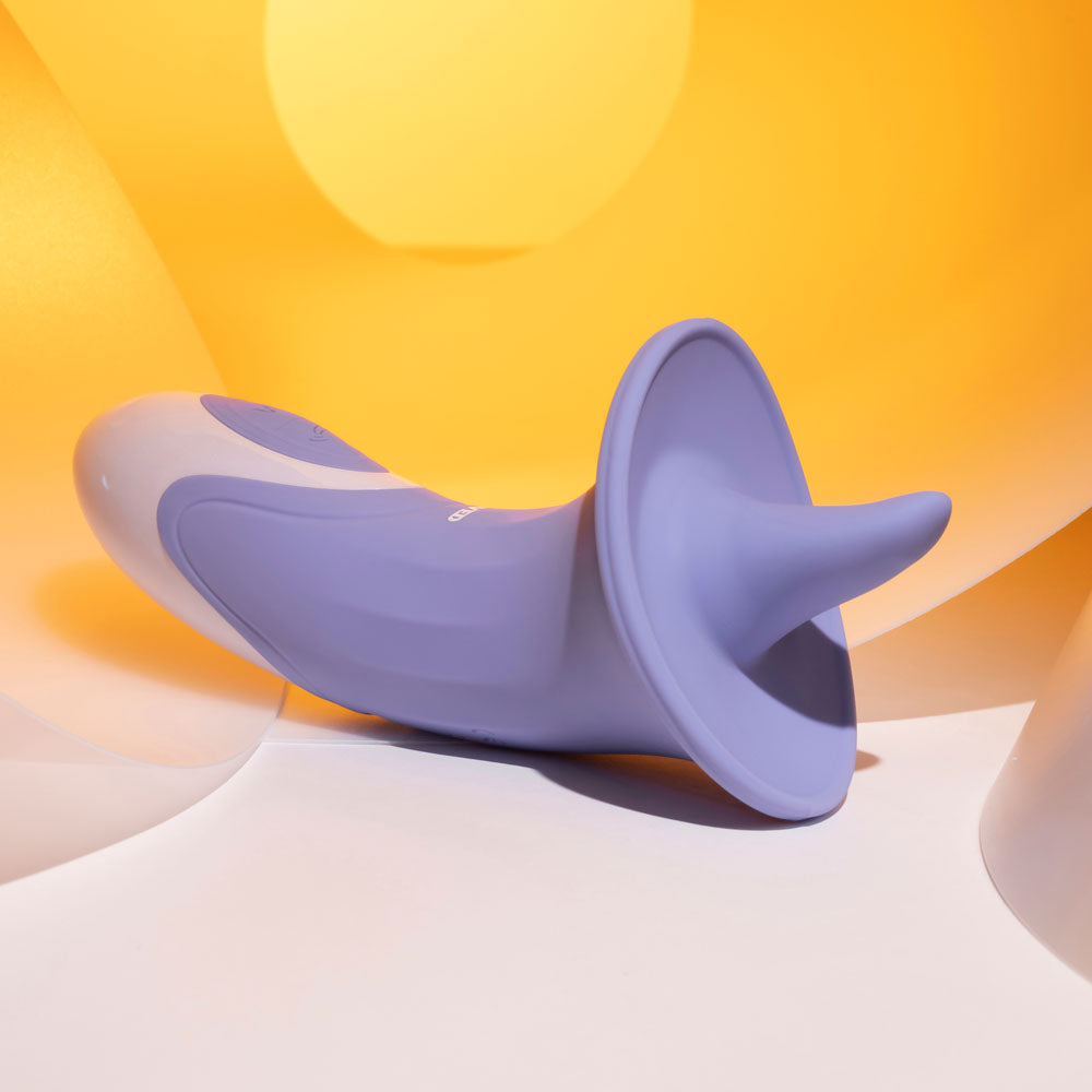 The Evolved LIX & KISSES is a purple, 18.7 cm ergonomic flicking tongue stimulator with customizable vibrating speeds, set against abstract yellow and white curves in soft lighting for a warm ambiance.