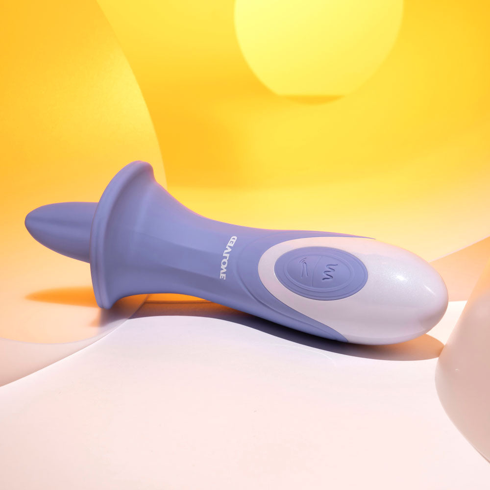 The Evolved LIX & KISSES, a purple 18.7 cm USB Rechargeable Flicking Tongue Stimulator, rests on a smooth surface with its curved tapering form and flared base hinting at an intriguing experience. Soft abstract yellow and white lighting creates a warm inviting atmosphere.