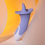 The Evolved LIX & KISSES is a lavender and white silicone device with a pointed, flared top in an ergonomic tongue-like shape. It rests against yellow and white curved surfaces, features buttons for speed adjustments, and is designed for personal use.