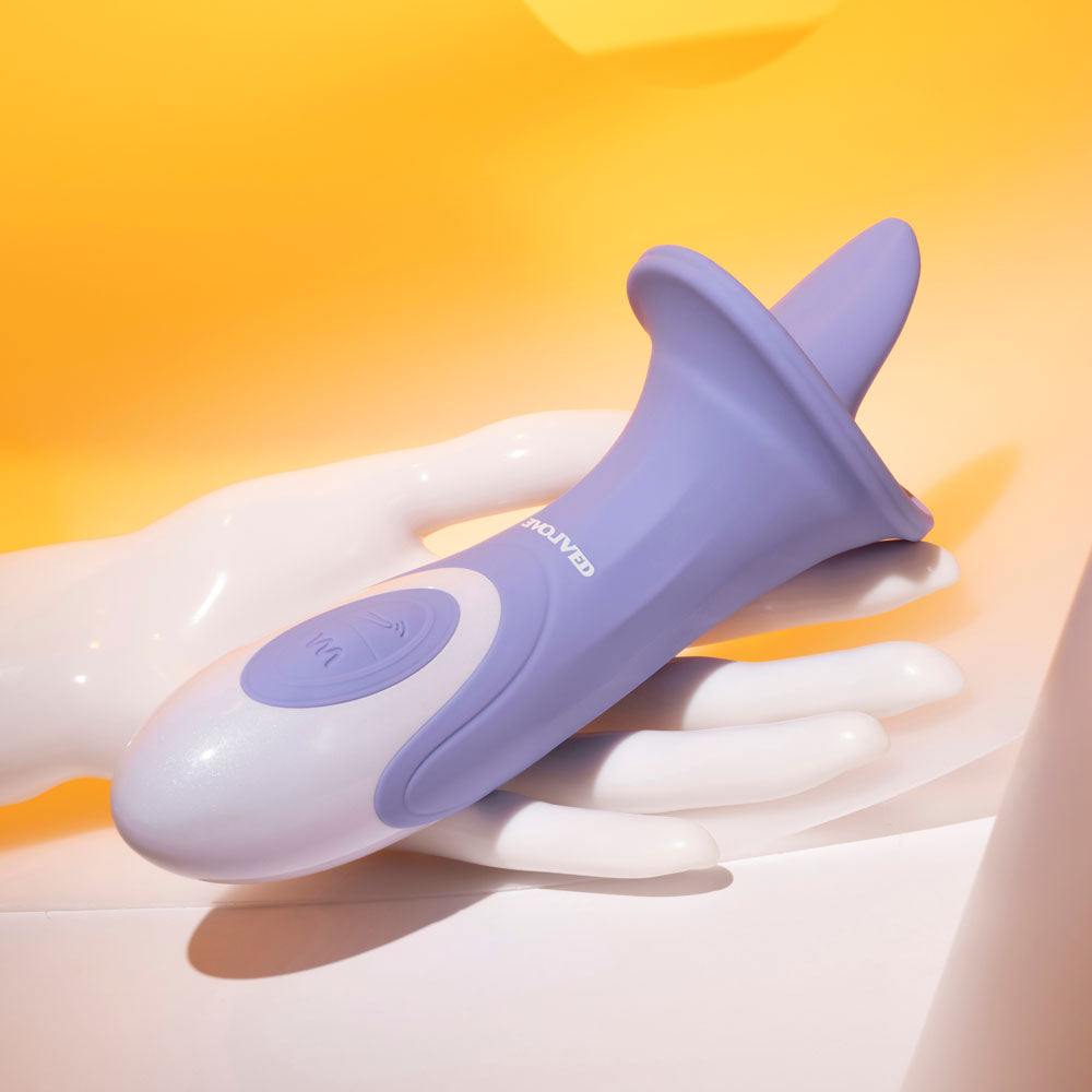 The Evolved LIX & KISSES - Purple 18.7 cm USB Rechargeable Flicking Tongue Stimulator, resembling a handheld massage device, is displayed in a white mannequin hand against a vibrant yellow backdrop. It features a curved tip and round power button, with soft shadows cast by the bright lighting.