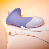 The Evolved LIX & KISSES - Purple 18.7 cm USB Rechargeable Flicking Tongue Stimulator rests on a warm-toned surface, connected to a white USB cable. Gentle lighting highlights its abstract curves and glossy finish, enhancing its resemblance to an oral experience simulator.