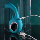 The Evolved HOW MANY LICKS - Blue 17.8 cm USB Rechargeable Vibrator, featuring a flicking stimulator and waterproof ergonomic design for G-Spot stimulation, is set against a reflective black surface amid transparent acrylic blocks against a teal background.