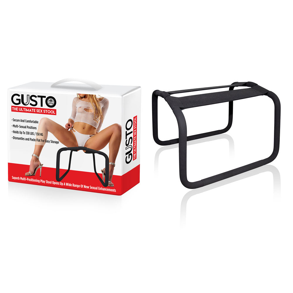 The Gusto - Black Position Stool is shown with its packaging, displaying an image of a woman in lingerie to hint at its use for intimate experiences. The stool has a rectangular frame with a fabric seat and hidden legs, offering versatility for various sexual positions.