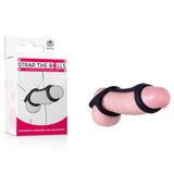 The packaging of the Strap The Balls - Black Cock Strap with Ball Stretcher showcases a pink and white design. Positioned on the left, it features its name. On the right, observe how it elegantly wraps around a realistic silicone model.