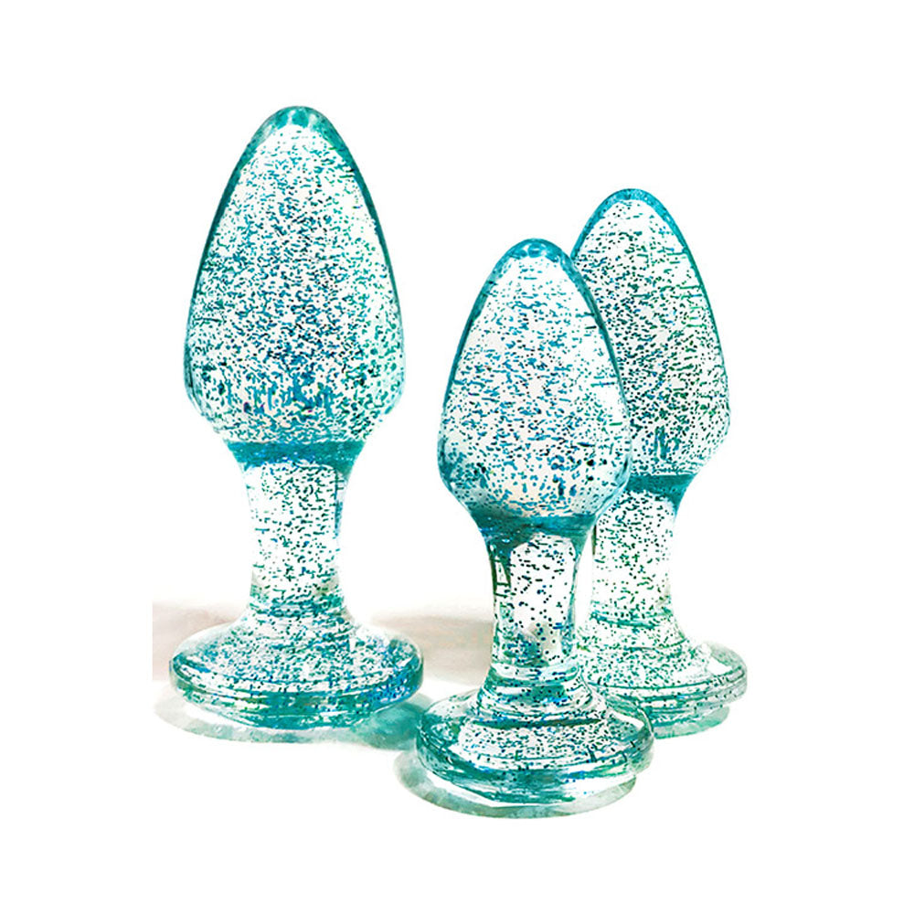 A set of three teal, transparent, gem-shaped objects stand on a white background. Resembling smooth cones with rounded tips and wide bases, each sparkles with specks of glitter. They are the Adam & Eve Glitter Gem 3-Piece Butt Plug Set in blue, available in three sizes.