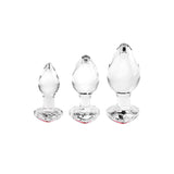 The Adam & Eve RED HEART GEM GLASS PLUG SET features three clear glass butt plugs arranged by size on a white background. Each plug has a teardrop-shaped top and a heart-edged, circular base, perfect for anal training or temperature play.