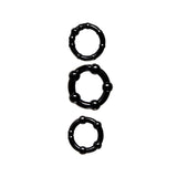 The Adam & Eve ADAMS PLEASURE KIT - Male Kit features three black, rubbery cock rings arranged vertically, increasing in size. Each ring has round beads of varying sizes evenly spaced around the circumference, creating a textured appearance against a plain white background.