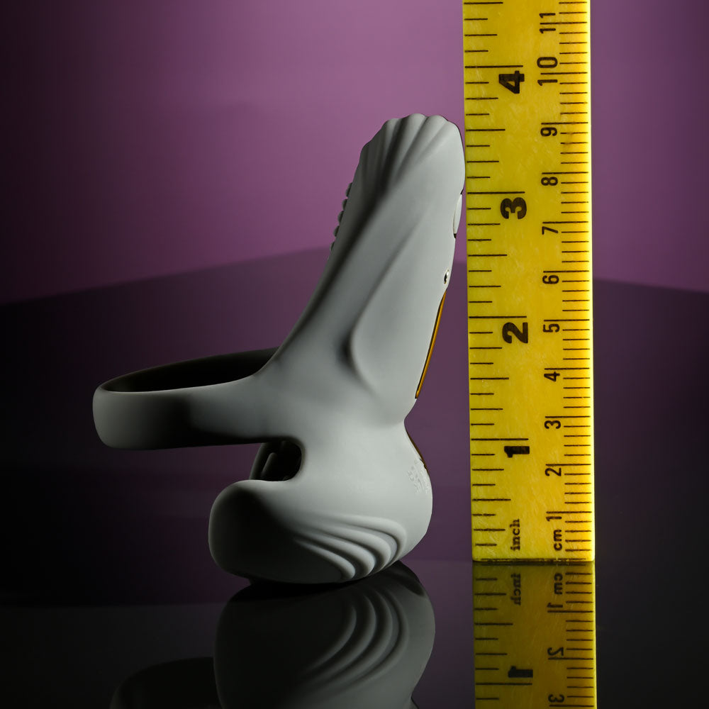 A grey Gender X UNDERCARRIAGE USB rechargeable vibrating ring is beside a yellow measuring tape with black markings. The purple gradient backdrop and glossy surface enhance its ergonomic, textured design.