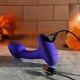 The Gender X ANYBODYS PLUG - Blue 11.4 cm USB Rechargeable Vibrating Butt Plug is connected to a USB cable on a textured surface, surrounded by sunflowers and a lit candle, creating a warm, inviting ambiance.