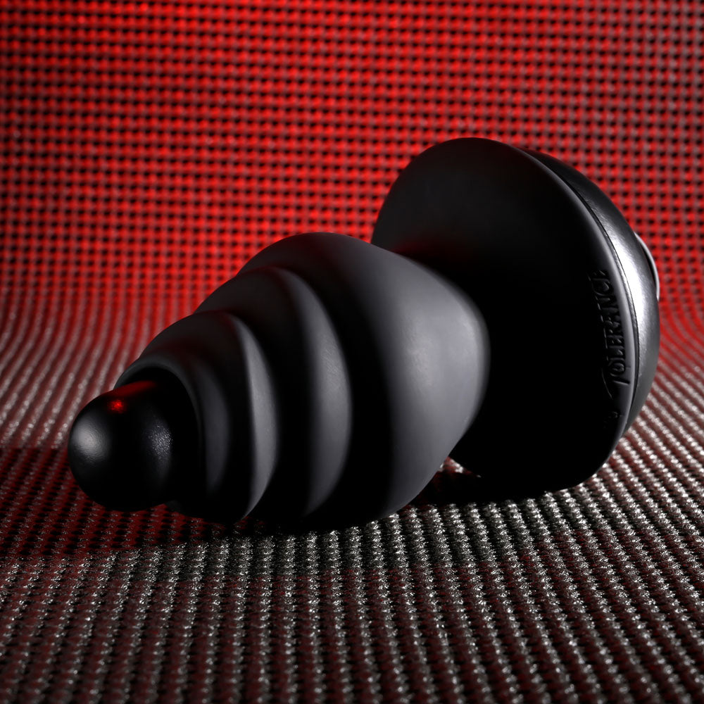 A black, spiral-shaped Gender X ECHO - Black USB Rechargeable Butt Plug with a wider base sits on a textured surface. The background shows a red, grid-like pattern with gradient effects for contrast. It has a matte finish and is made of silicone, featuring waterproof and submersible design.