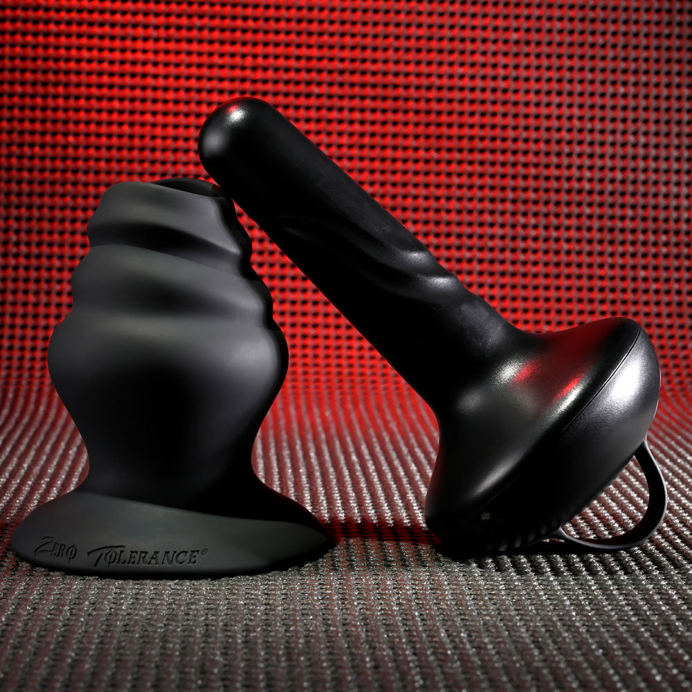 A black silicone adult toy is displayed against a textured red-hued backdrop. It features the Gender X ECHO - Black 15.3 cm USB Rechargeable Butt Plug with a smooth, cylindrical design and wide base. The background highlights its sleek, matte black finish.