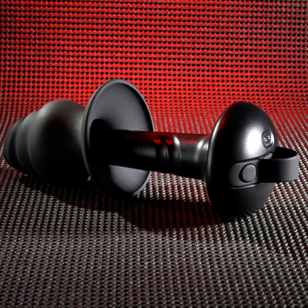 Close-up of a sleek, futuristic black Gender X ECHO USB Rechargeable Butt Plug on a textured surface. A vibrant red light casts reflections on its matte finish, highlighting its contours. The design includes waterproof and submersible features.