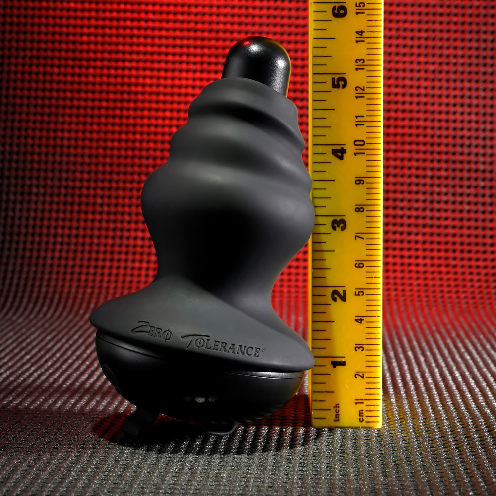 A black, ridged object with Zero Tolerance stands upright against a yellow measuring tape, indicating a height of about 5 inches. This Gender X ECHO - Black 15.3 cm USB Rechargeable Butt Plug is set against a textured red and black background, showcasing its sleek design.