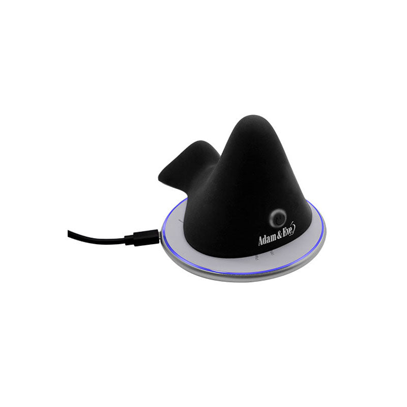 The Adam & Eve THE RUMBLING RIDER is a black, conical-shaped silicone massager on a round charging base with a cable. The base emits a subtle blue light ring and features dual motors with the Adam & Eve logo and circular design.