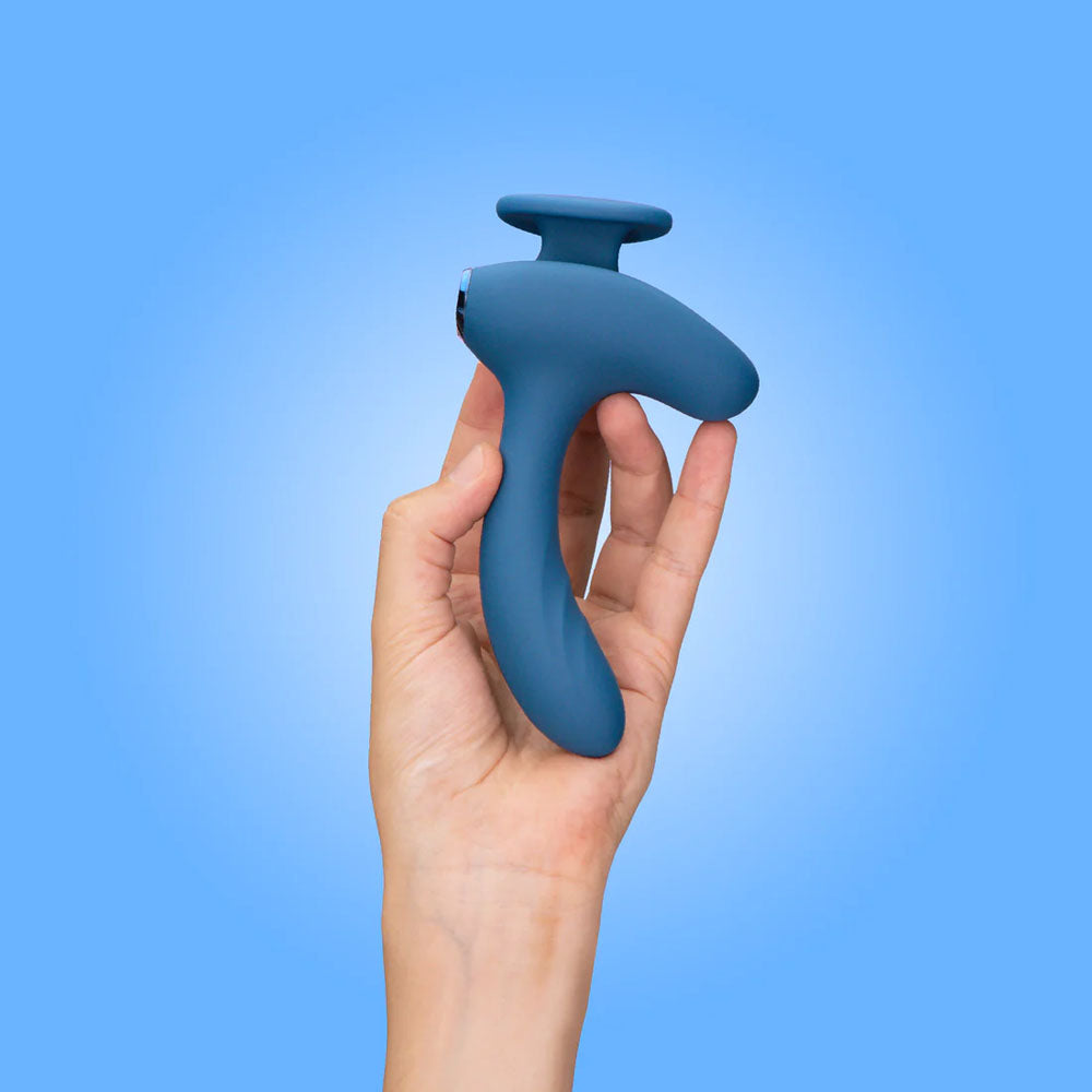 A hand holds the JimmyJane Solis Kyrios, a sleek, ergonomic blue prostate massager with dual motors and a matte finish. Set against a light blue background, it features a comfortable handle-like grip and comes with USB rechargeability and a remote for ease of use.